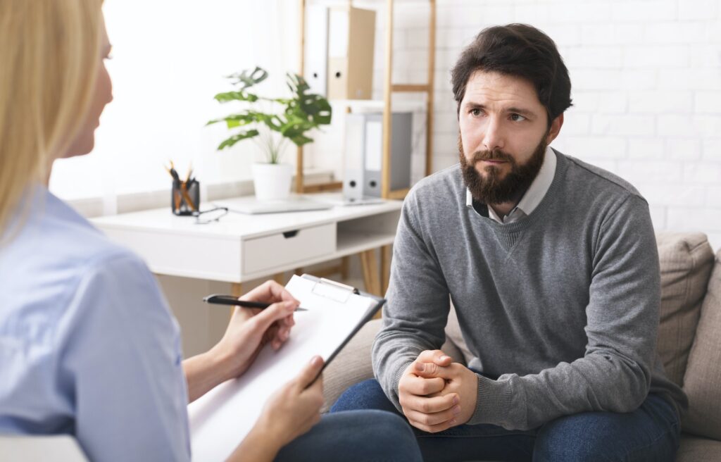 Stressed young man talking to psychologist at therapy
